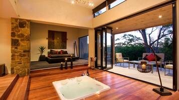 A spacious room with a large bathtub, a cozy seating area with a sofa and chairs, and a view of the outdoors through large glass doors.