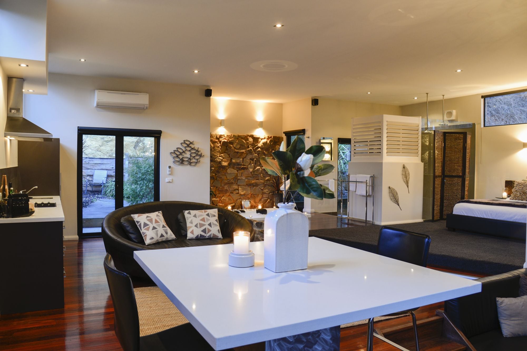 Un salón moderno con una mesa blanca, sofá de cuero negro y una pared de piedra.