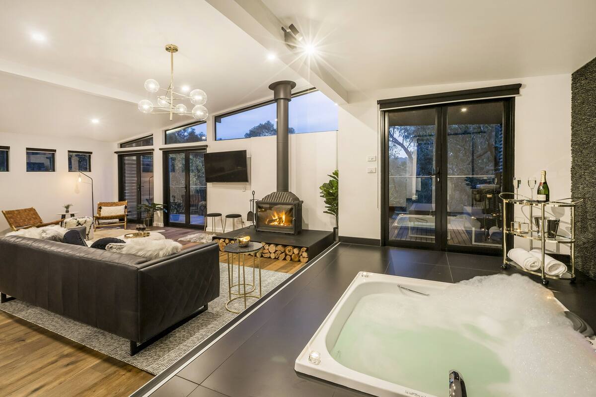 A modern living room with a fireplace, a large sofa, a coffee table, and a hot tub.