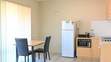 A compact kitchen with a refrigerator, microwave, and a small dining table with chairs.