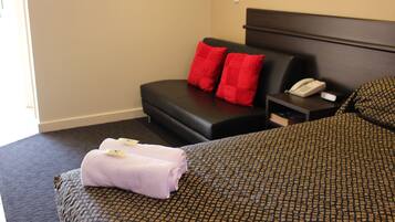 A hotel room with a bed, a small sofa, a nightstand with a phone, and red pillows.