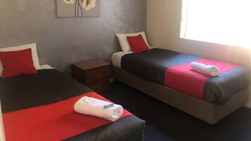 A hotel room with two beds, each with a red and white pillow, a small wooden nightstand, and a red towel on the bed.