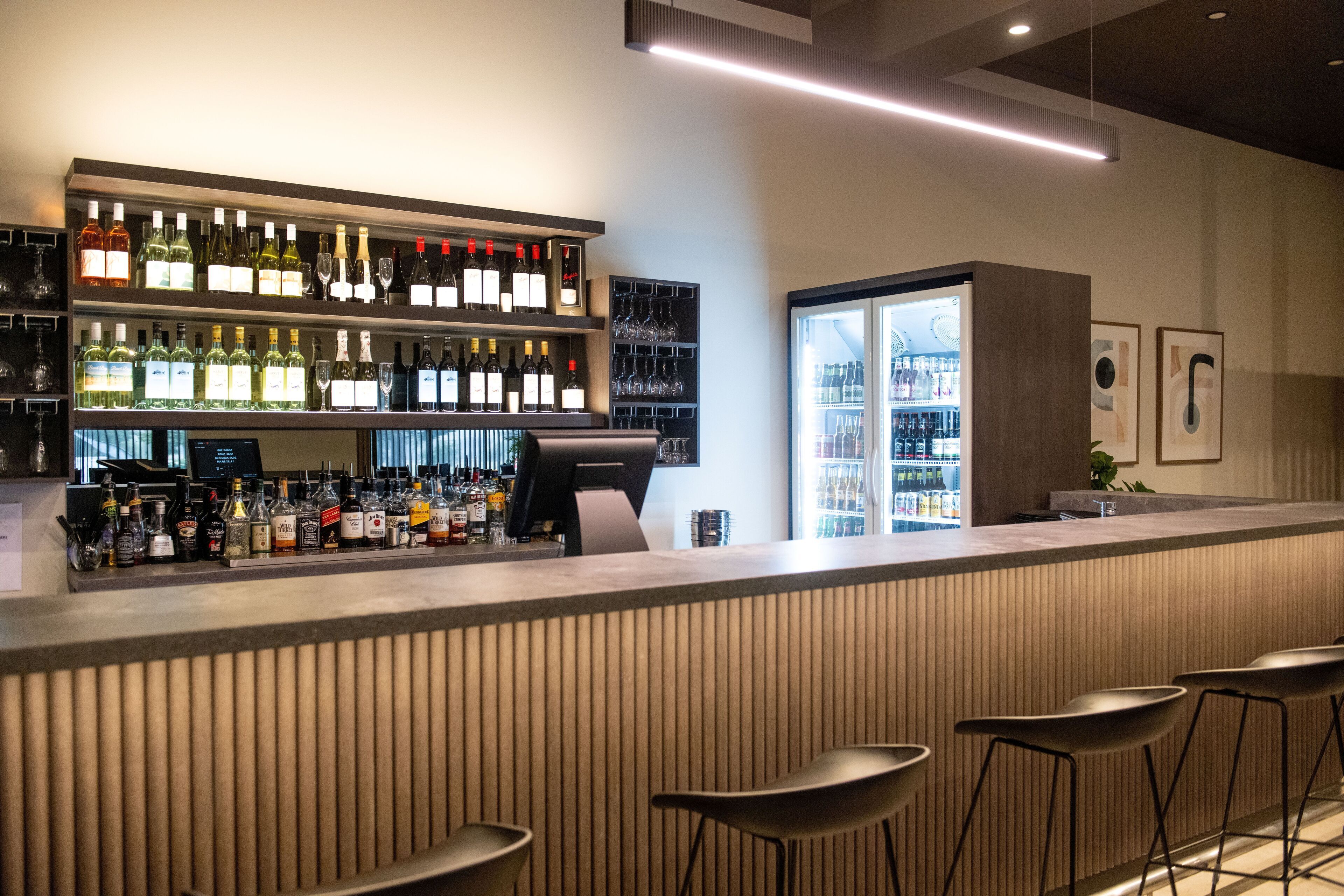 A bar area with shelves of liquor bottles, a refrigerated display, and bar stools.