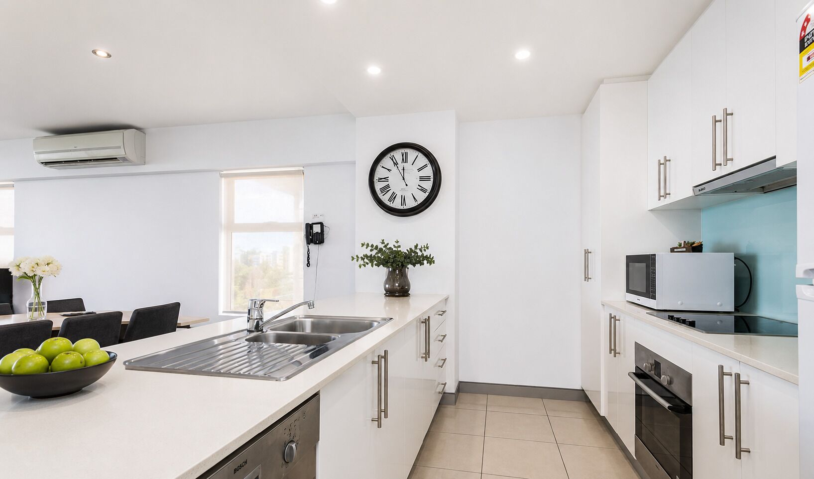 Una cocina moderna con armarios blancos, un lavavajillas Bosch, un microondas y un reloj en la pared.