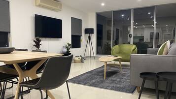 A modern living room with a dining area, a green armchair, and a grey sofa.