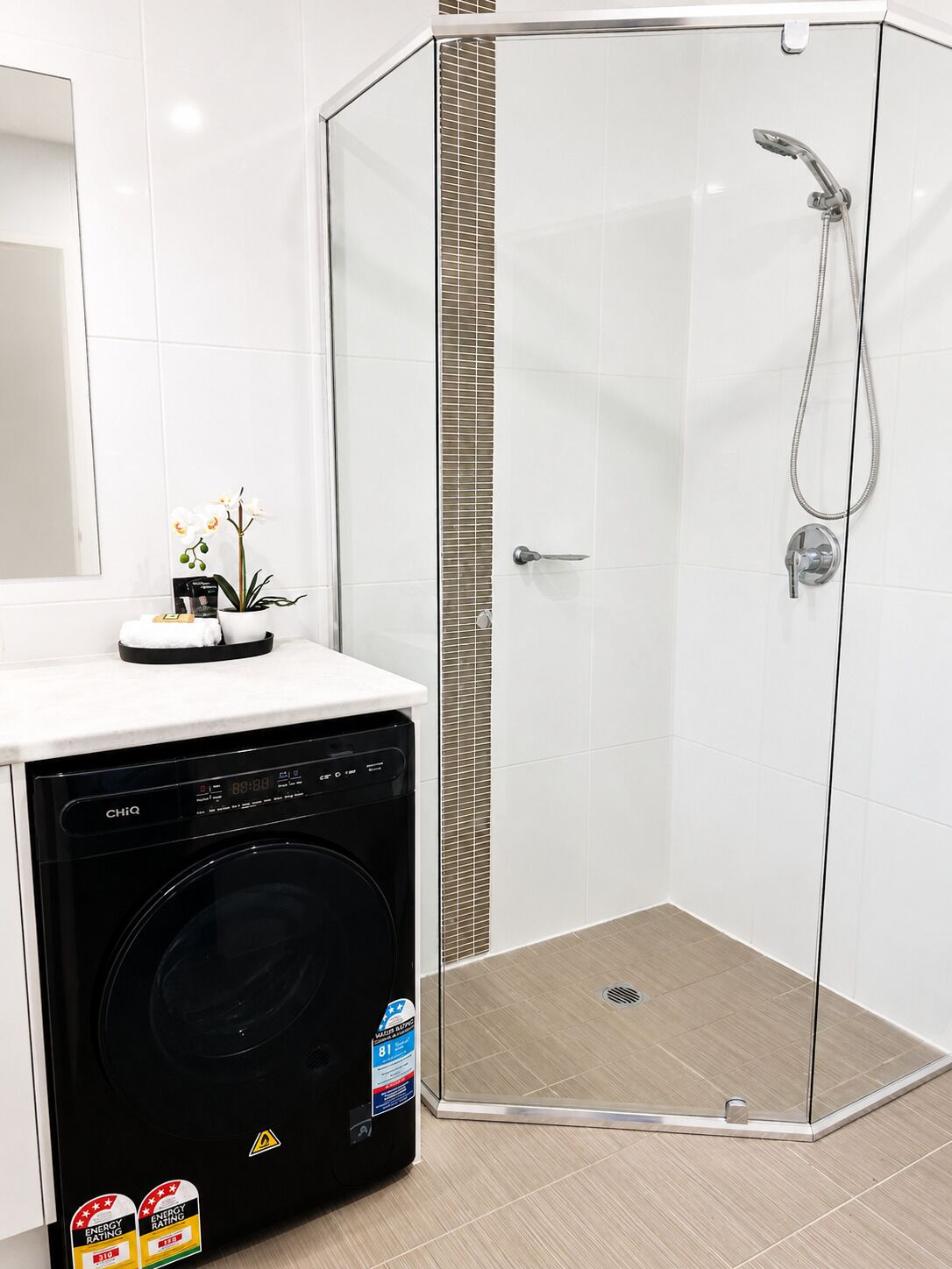 A modern bathroom with a glass shower enclosure, a washing machine, and a potted orchid.