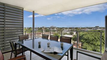 A balcony with a table and chairs, overlooking a cityscape with buildings and greenery.