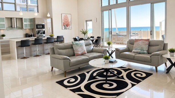 A spacious living area with a modern kitchen, large windows, and a balcony with a view of the sea. - Redvue Apartments (Redcliffe)