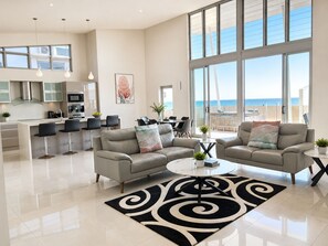 A spacious living area with a modern kitchen, large windows, and a balcony with a view of the sea. - Redvue Apartments (Redcliffe)