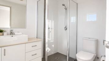 A modern bathroom with a glass-enclosed shower, a white toilet, and a vanity with drawers.