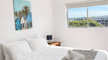 Habitación de hotel con cama, ventilador de techo, ventana con vistas y un cuadro en la pared.