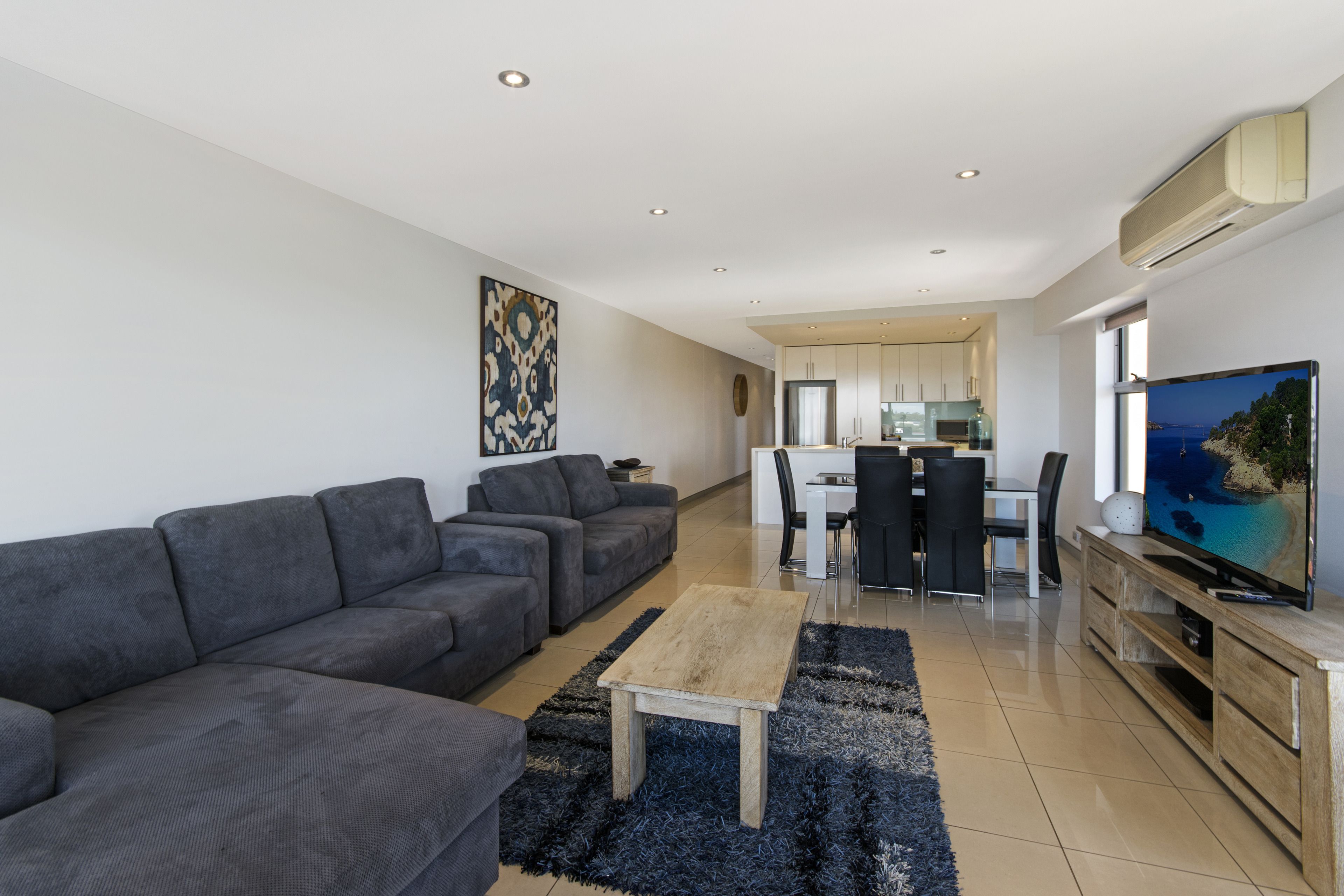 A modern living room with a grey sectional sofa, a wooden coffee table, and a flat-screen TV on a wooden stand.