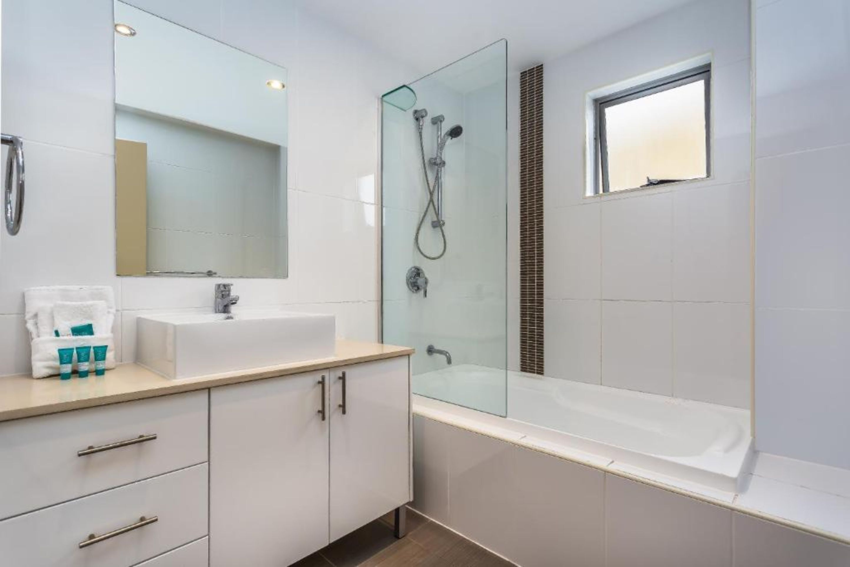 Un baño moderno con ducha envuelta en vidrio, un espejo grande, un lavamanos blanco y una ventana.