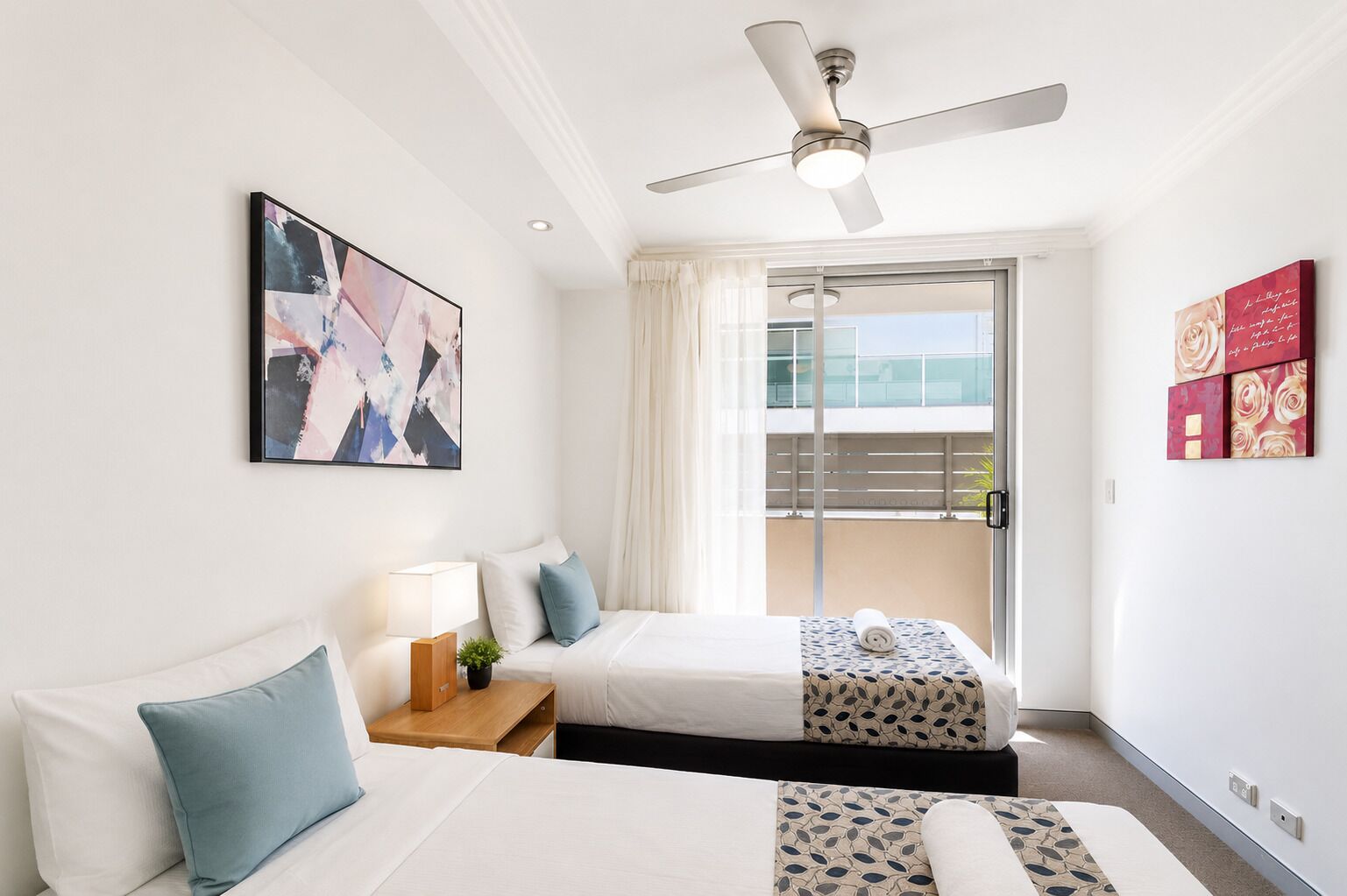A hotel room with two beds, a ceiling fan, a large window with curtains, and a balcony with a view.