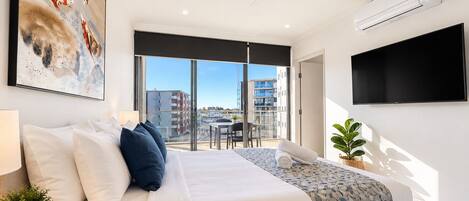 Una habitación de hotel moderna con una cama, un ventilador de techo, un televisor de pantalla plana y un ventanal con vistas a la ciudad.