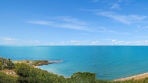 A coastal view with a beach, clear sky, and a small pavilion. - Redvue Apartments (Redcliffe)