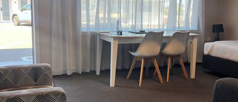 A hotel room with a desk, two chairs, a bed, and a patterned armchair.