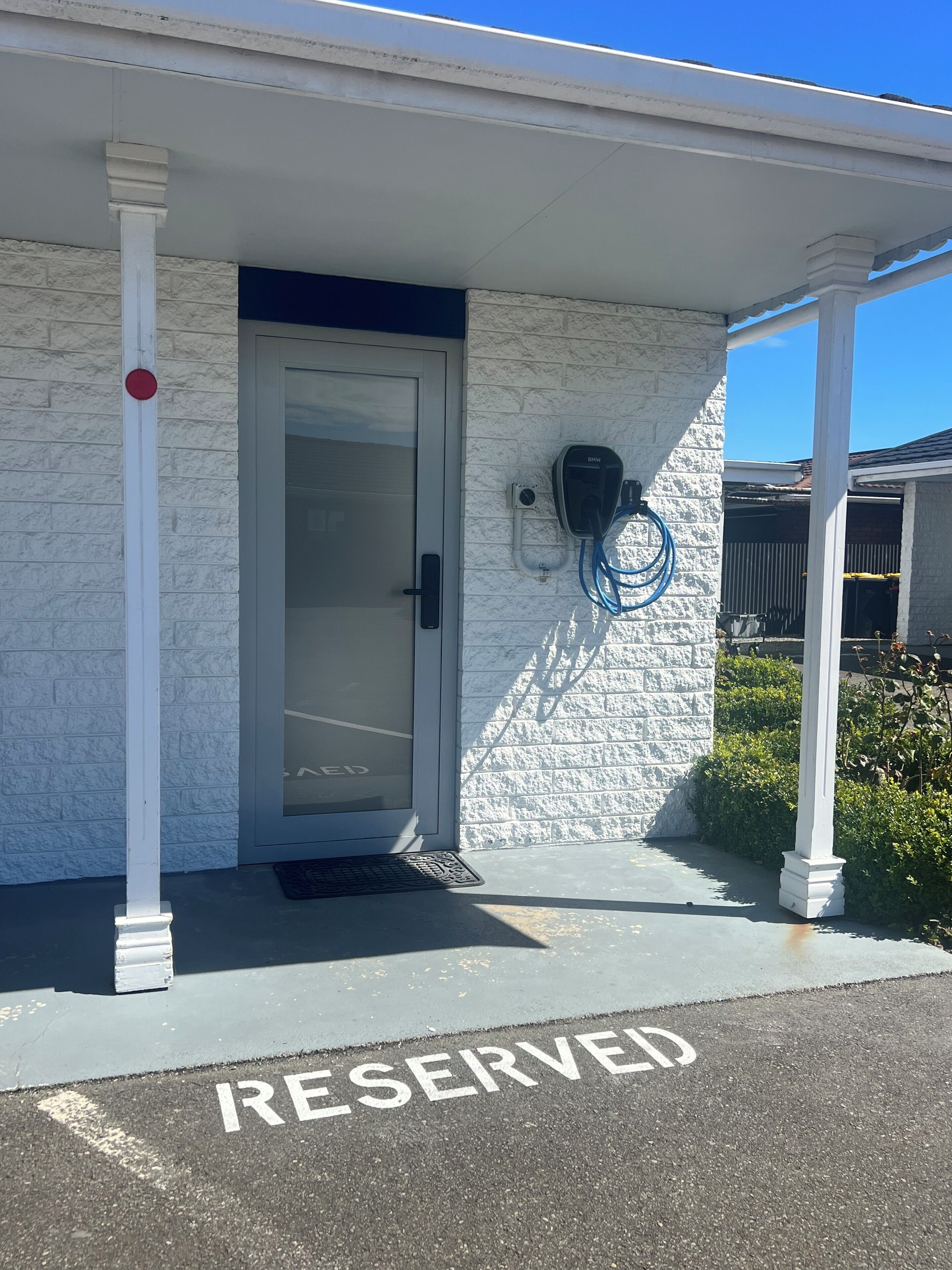 Entrada de un edificio con un letrero de estacionamiento reservado, una puerta y una estación de carga para vehículos eléctricos.