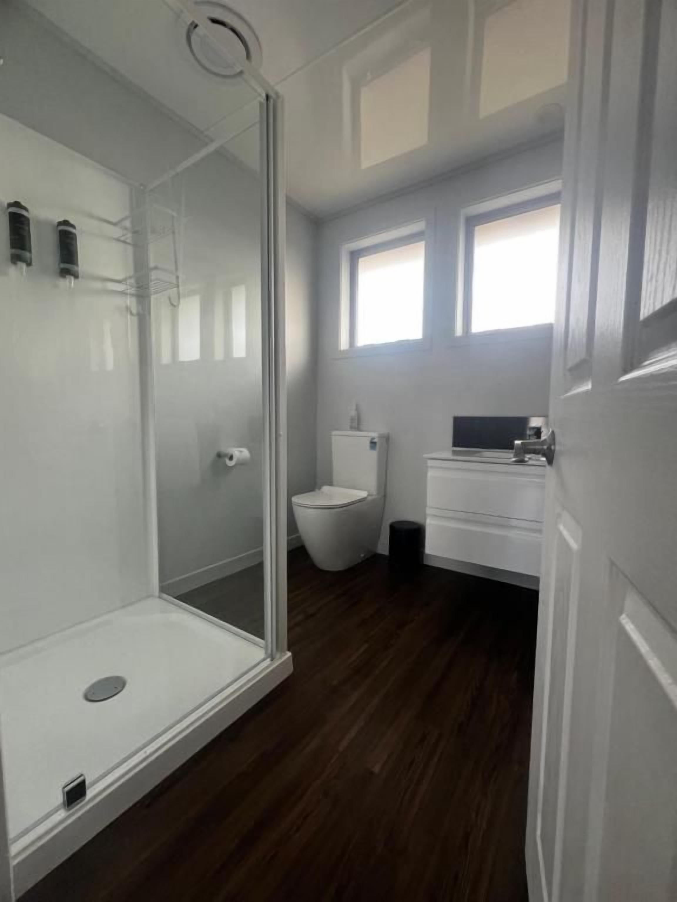 A bathroom with a glass-enclosed shower, a toilet, and a sink area.