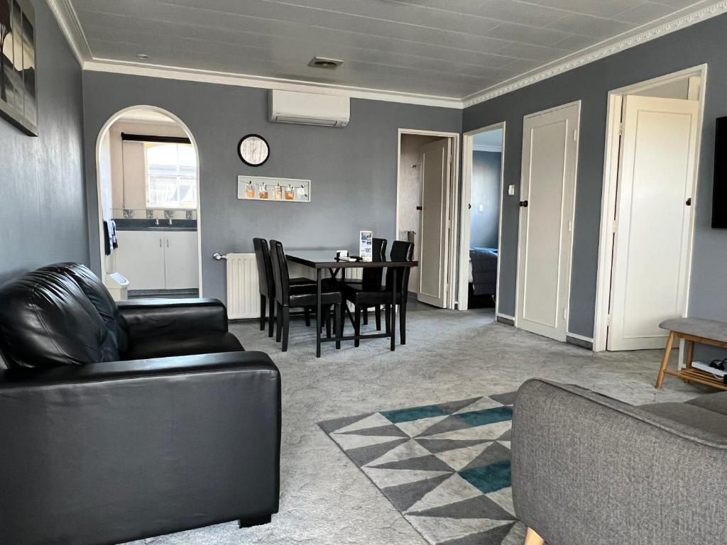 A living room with a sofa, a coffee table, and a dining area with chairs. There is a kitchen visible in the background.
