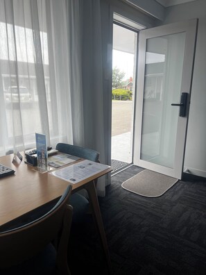 Ein Hotelzimmer mit Schreibtisch aus Holz, einem Stuhl, einer Glastür und Blick ins Freie.