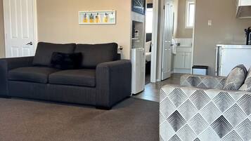 A living room with a grey sofa, a patterned sofa, a clock, and a wall-mounted air conditioner.