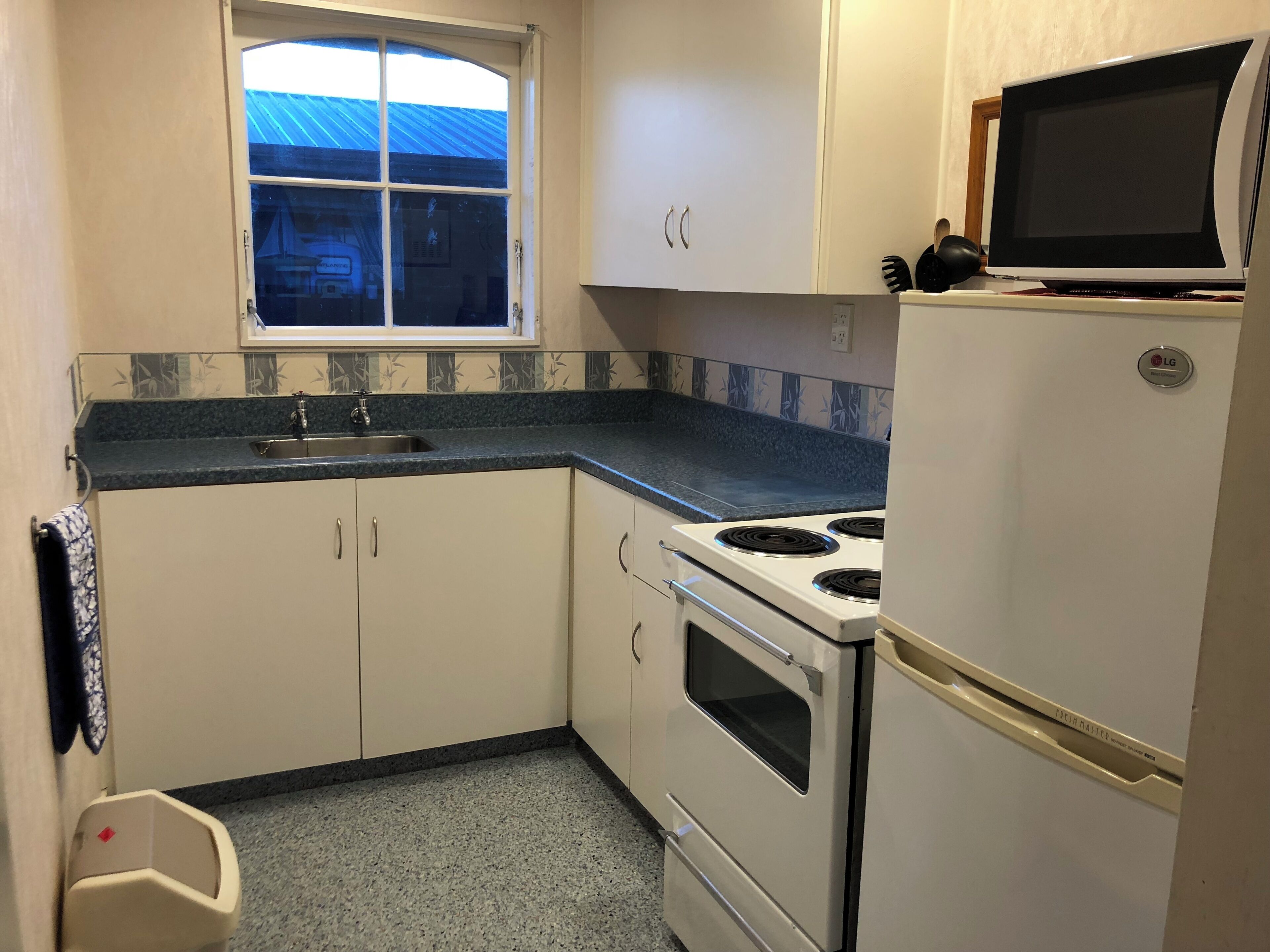 A compact kitchen with a window, a sink, a stove, and a refrigerator.