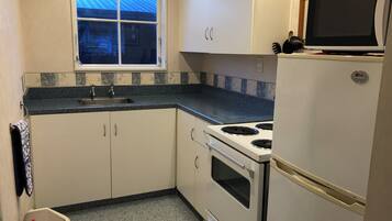 A compact kitchen with a window, a sink, a stove, and a refrigerator.