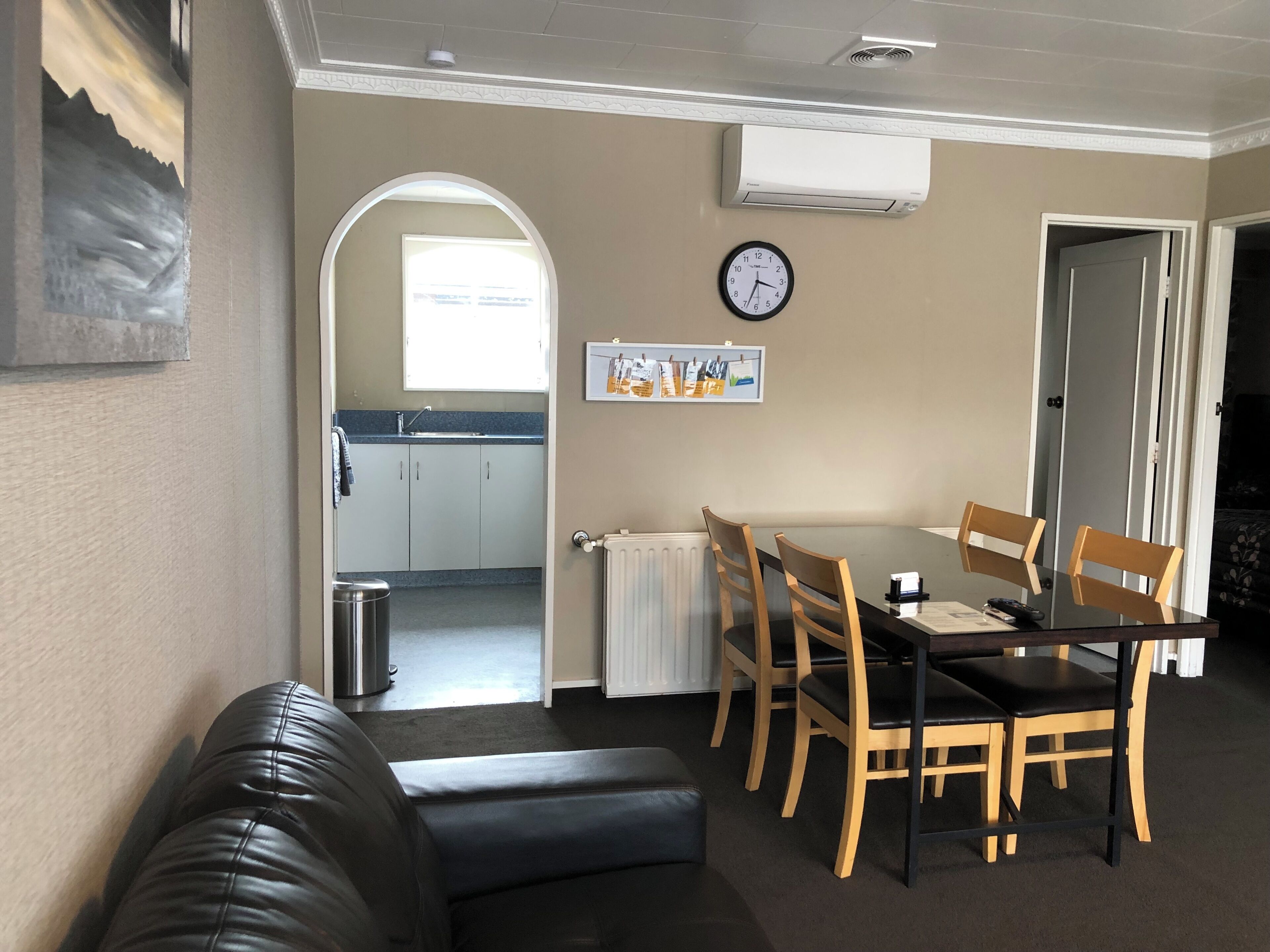 A dining area with a table and chairs, a clock on the wall, and a view into the kitchen.