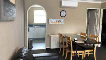 A dining area with a table and chairs, a clock on the wall, and a view into the kitchen.