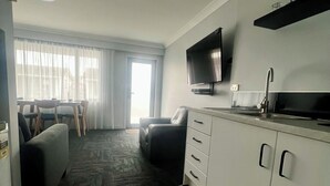 Una habitación de hotel moderna con sala de estar, kitchenette y un ventanal con cortinas.