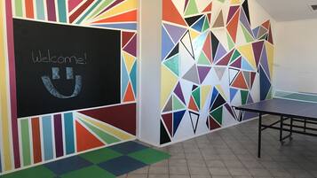 A room with a colorful geometric wall design, a welcome sign, and a ping pong table.