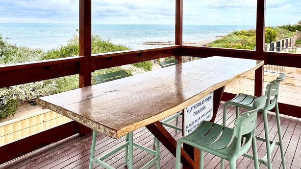 Un espacio de estar al aire libre con techo, con una mesa y sillas de madera, con vista a la playa.
