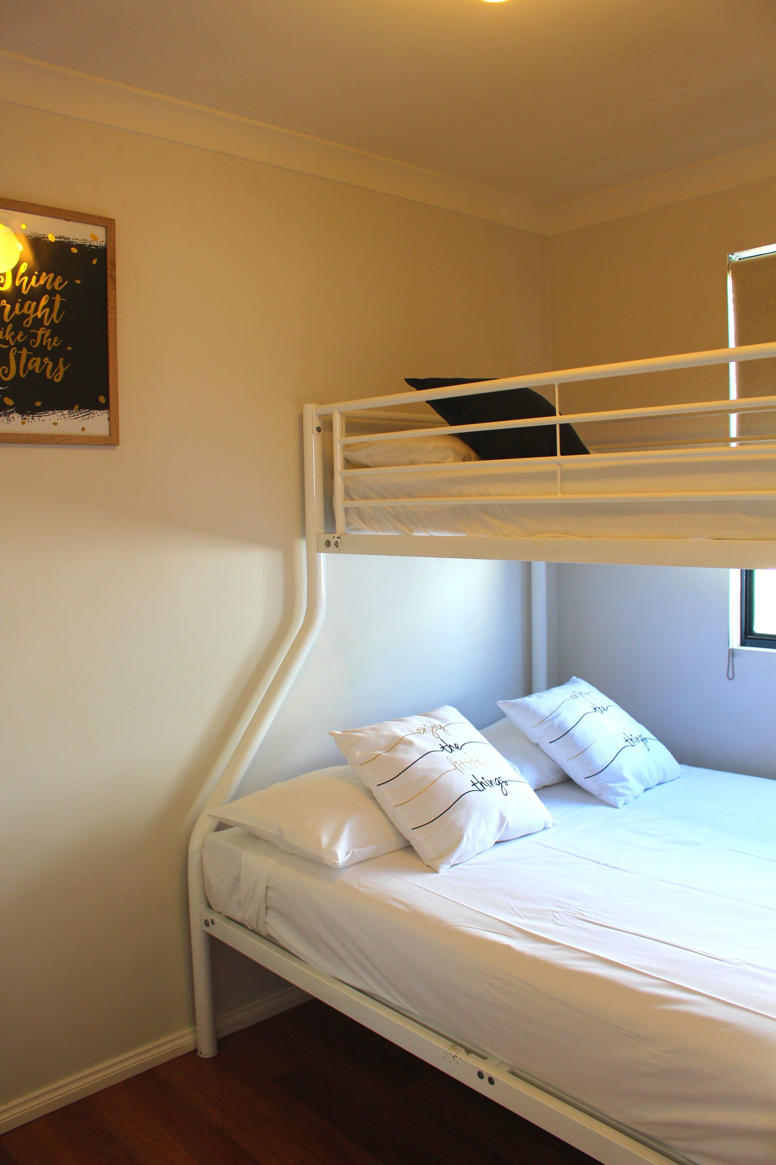 A bunk bed with white bedding and pillows, a framed quote on the wall, and a window to the right.