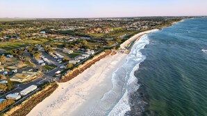 Vista aérea de una zona costera con una playa arenosa, un vecindario residencial y una vista despejada del océano.