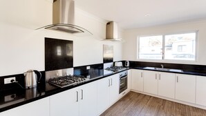 Una cocina moderna con armarios blancos, encimeras negras, electrodomésticos de acero inoxidable y un ventanal que proporciona luz natural.