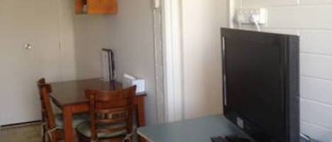 A compact room with a dining table and chairs, a television, and a small refrigerator.