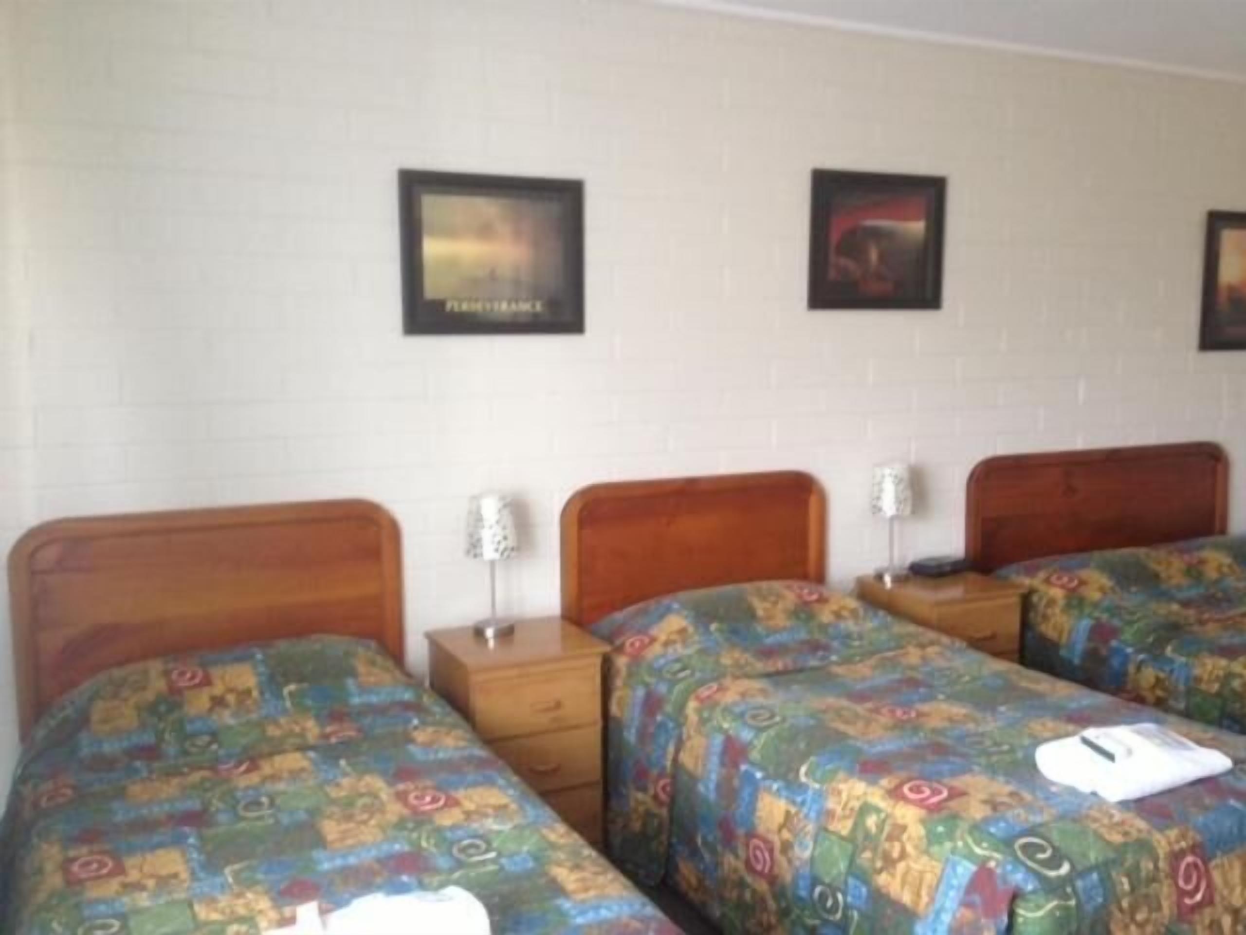 A hotel room with two wooden beds, a nightstand, and a wall-mounted lamp.