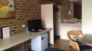 A room with a brick wall, a small white refrigerator, a television, a wicker chair, and a painting of sunflowers. - Gisborne Motel (Gisborne)