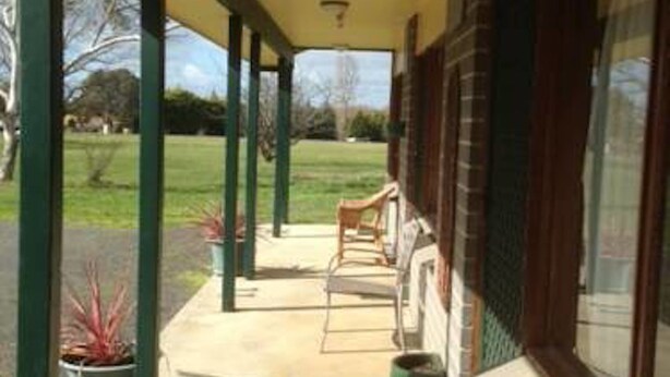 A covered porch with chairs and potted plants, a brick wall, and a view of a grassy area. - Gisborne Motel (Gisborne)