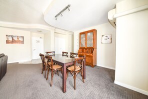 A dining room with a rectangular table and six chairs, a wooden cabinet, and a door with a picture on the wall. - Founda Gardens Apartments (Auchenflower)