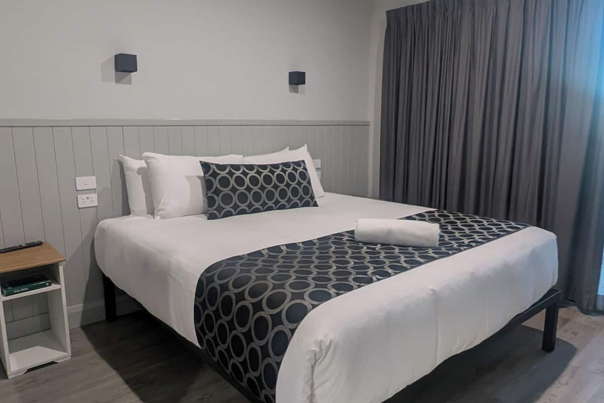 A modern hotel room with a large bed, a bedside table, a wall-mounted light, and a window with curtains.