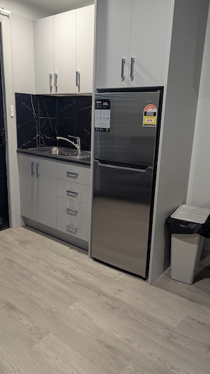 Cozinha moderna com armários brancos, geladeira de aço inoxidável e painel de parede em mármore preto.
