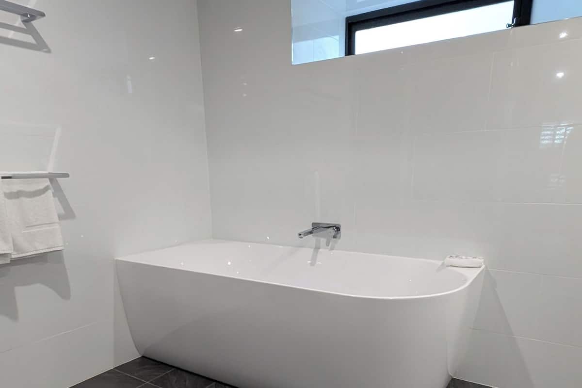 A modern bathroom with a freestanding bathtub, dark tiled flooring, and a small window above the tub.