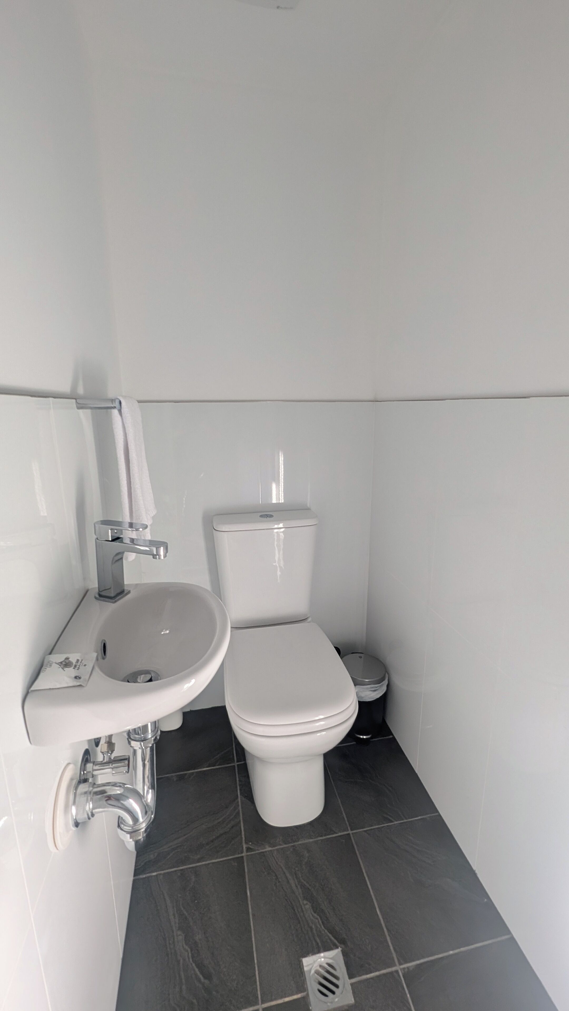 A small, clean bathroom with a toilet, sink, and a trash bin.