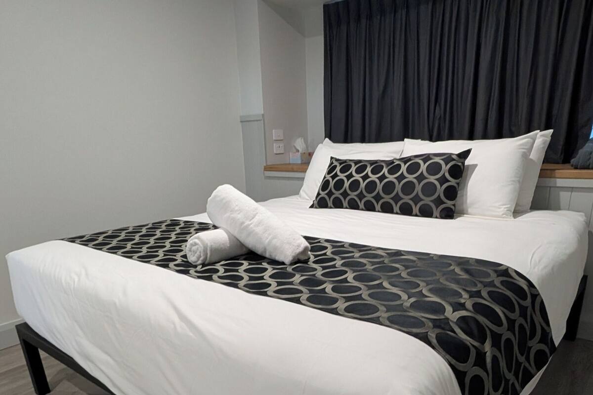 A modern hotel room with a large bed, a wooden floor, and a dark curtain.