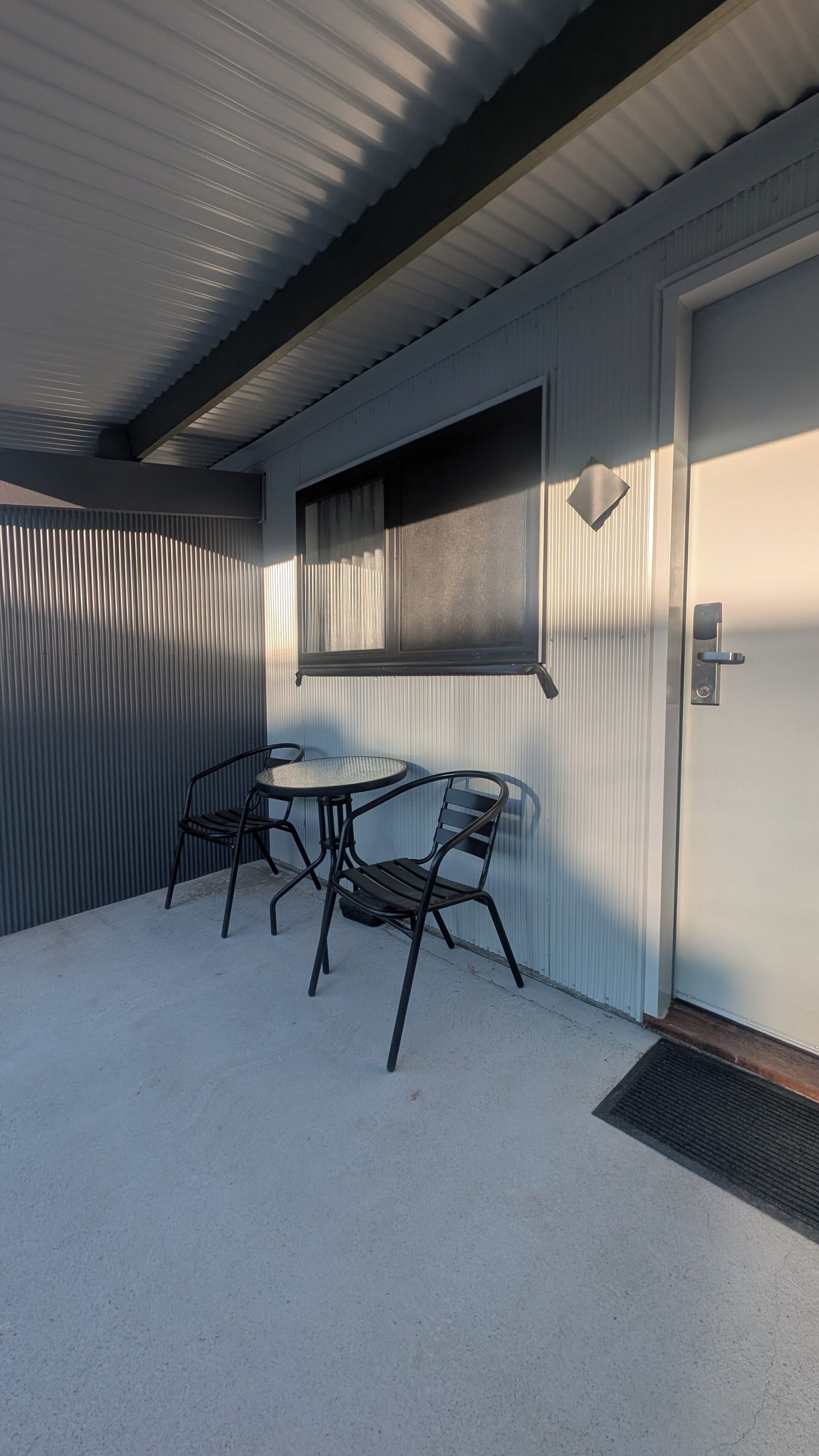 Un espacio de estar al aire libre techado con una mesa, sillas, una ventana y una puerta.