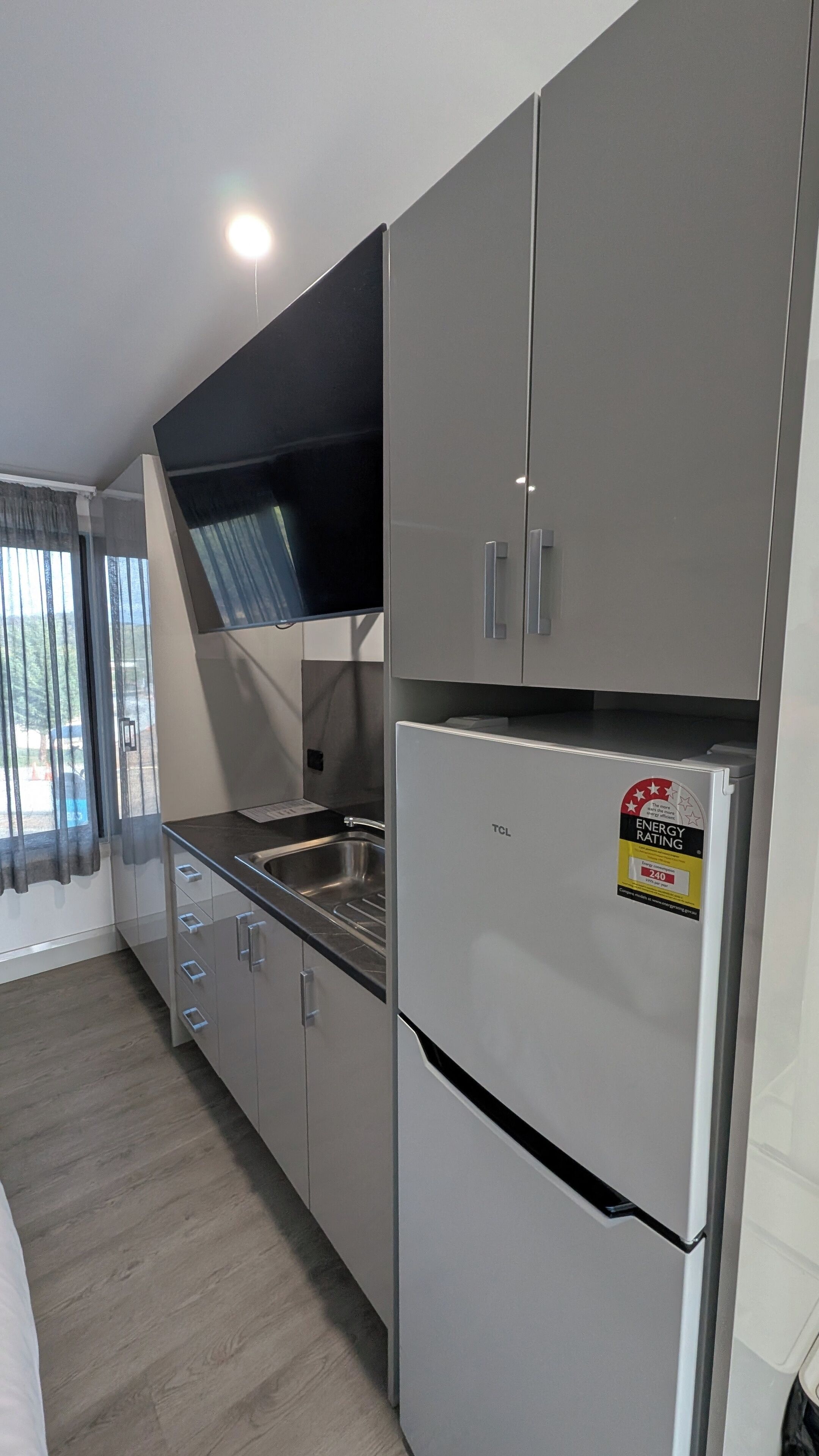 A modern kitchen with grey cabinets, a stainless steel sink, and a refrigerator with an energy rating sticker.
