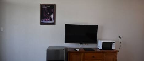 A kitchenette with a refrigerator, microwave, and a flat-screen TV mounted on the wall.