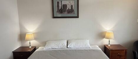 Habitación de hotel con una cama grande, dos mesitas de noche con lámparas, un cuadro en la pared y una silla.